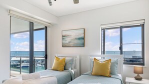 Ein Hotelzimmer mit zwei Betten, großen Fenstern, einem Gemälde und Blick auf den Hafen.