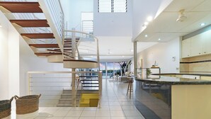 A spacious, modern interior with a central staircase, a kitchen area, and a seating area with a view.