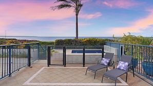 A balcony with two lounge chairs and a small pool, overlooking the ocean.