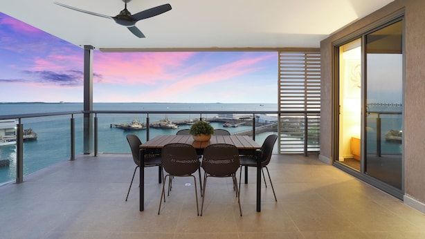 Un balcon avec une table et des chaises, un ventilateur de plafond et une vue sur la mer et les bateaux.
