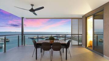 Un balcon avec une table et des chaises, un ventilateur de plafond et une vue sur la mer et les bateaux.