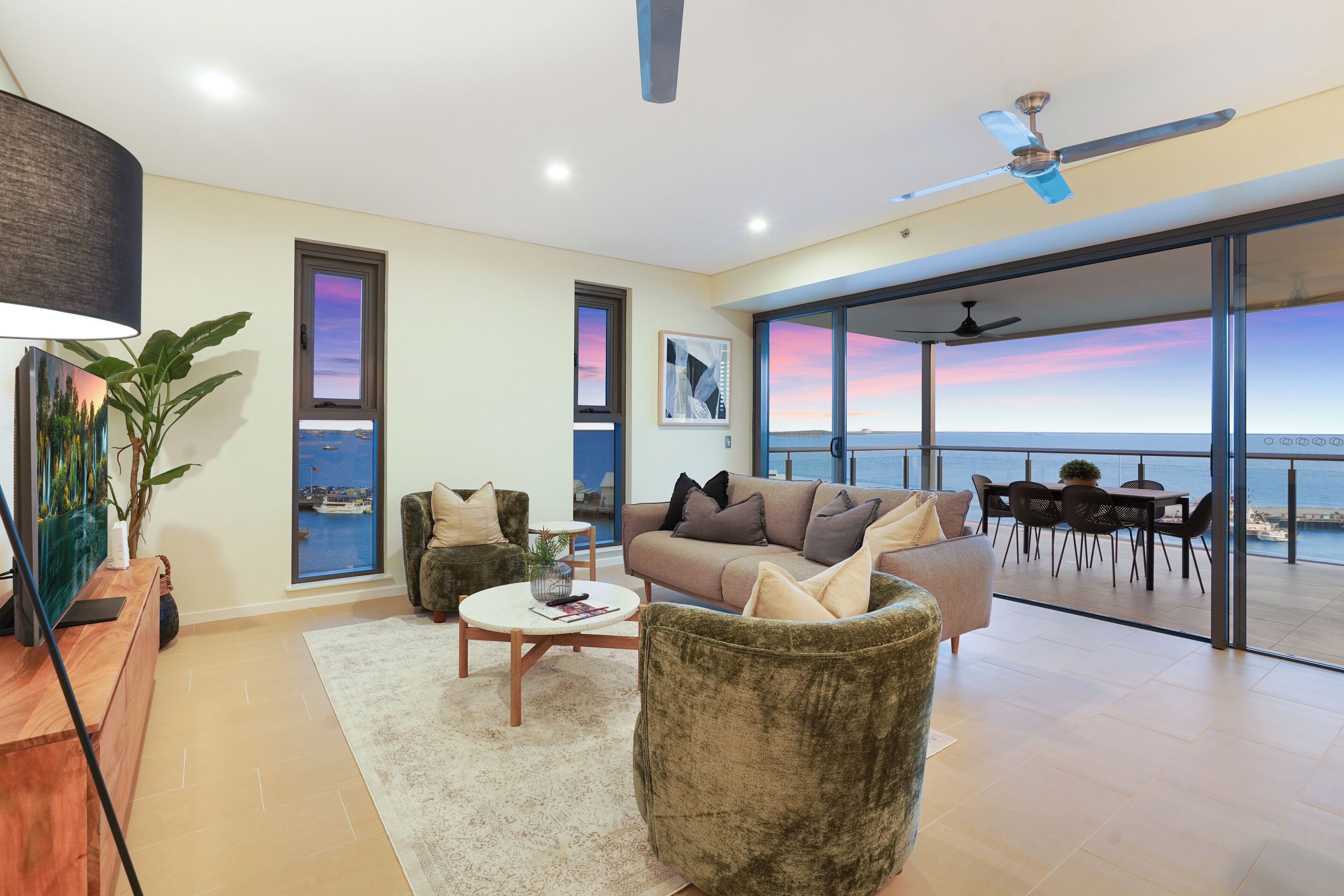 Un salon moderne doté d’une grande fenêtre donnant sur la mer, d’un ventilateur de plafond et d’un coin repas avec vue.