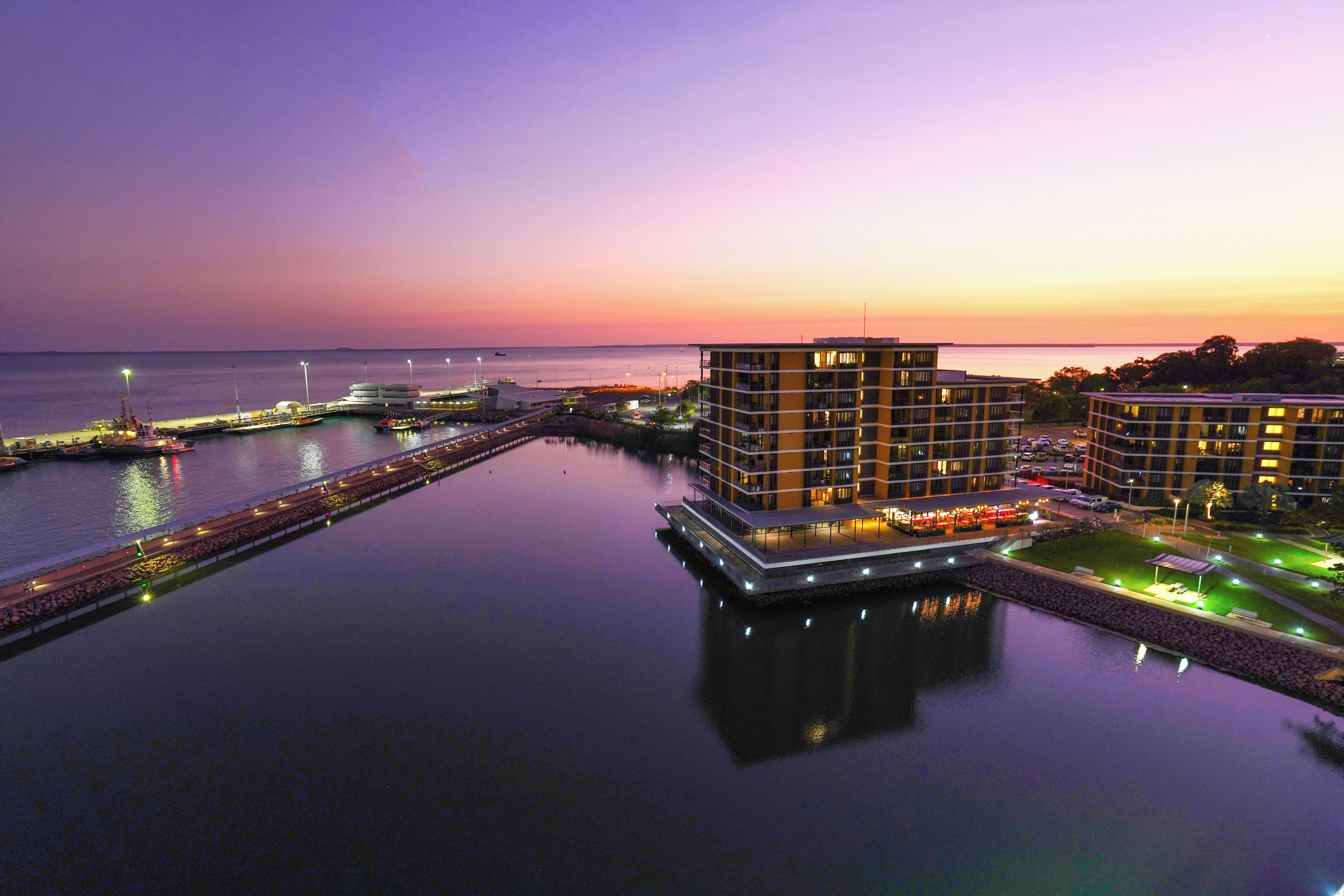 A waterfront hotel with a modern design, featuring a central building with multiple floors and a flat roof.