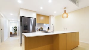 Une cuisine moderne dotée d’un grand îlot central, d’appareils électroménagers en acier inoxydable, de meubles en bois et d’un luminaire suspendu.