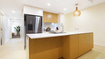 Une cuisine moderne dotée d’un grand îlot central, d’appareils électroménagers en acier inoxydable, de meubles en bois et d’un luminaire suspendu.