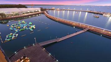 A waterfront area with a dock, a floating structure with slides, and a building with a large roof.