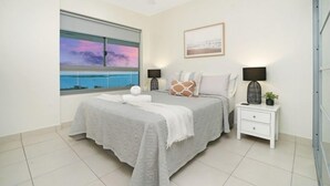 A bedroom with a bed, nightstands, a ceiling fan, a window with a view, and a framed picture on the wall.
