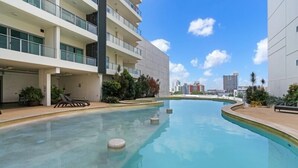 A modern building with a swimming pool, balconies, and a clear sky.