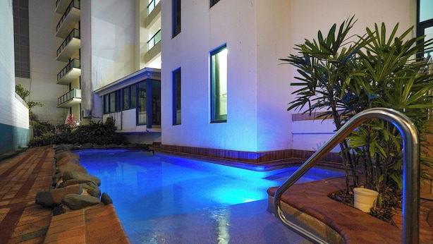 Uma piscina interior com borda revestida de azulejos, corrimão de metal e um vaso de planta perto da borda da piscina.