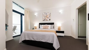 Quarto moderno com uma cama grande, luminárias laterais, uma obra de arte na parede e vista através de uma porta de vidro.