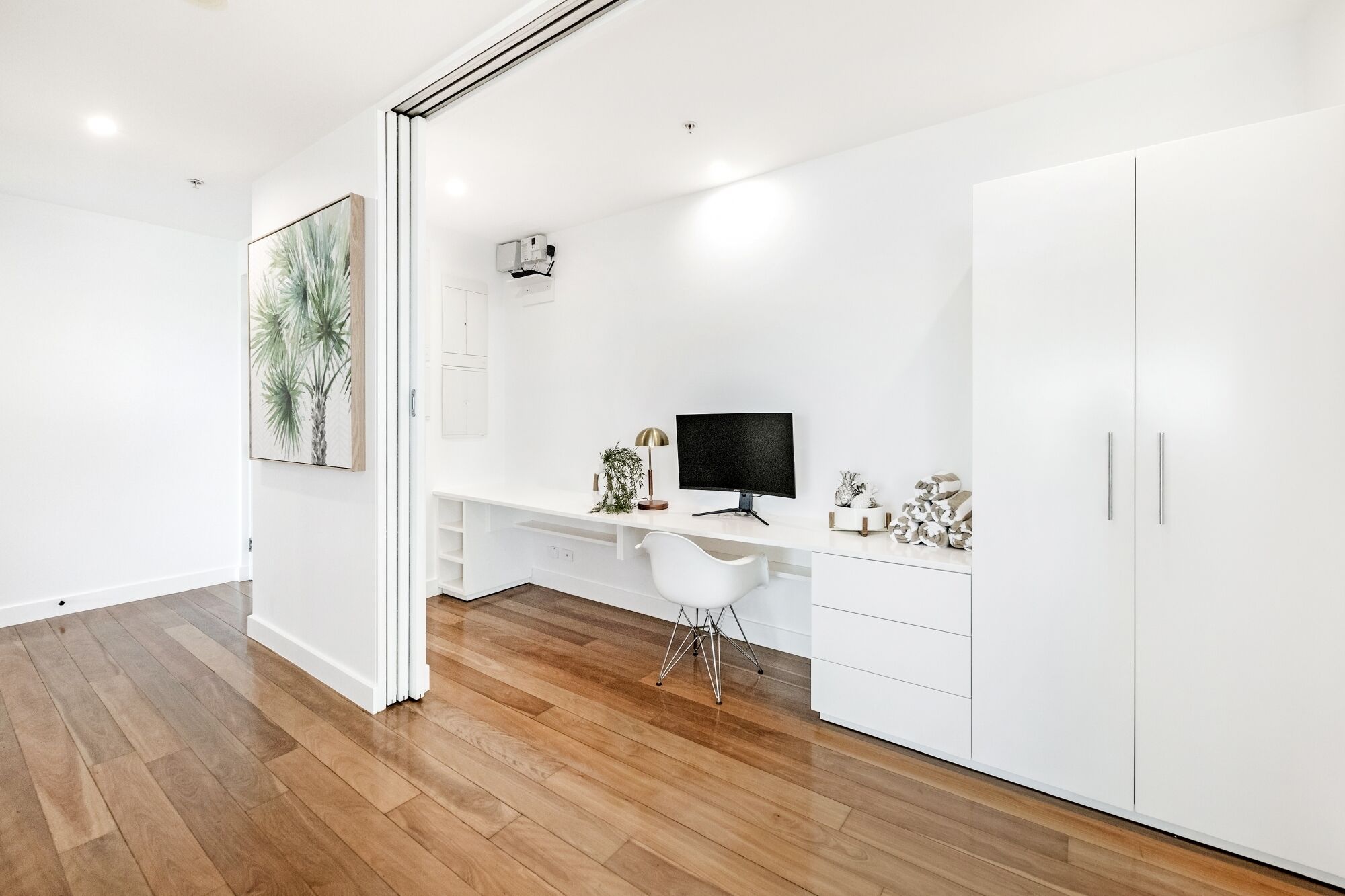 A modern, white-themed office space with a wooden floor, a desk with a computer, a chair, and a cabinet.