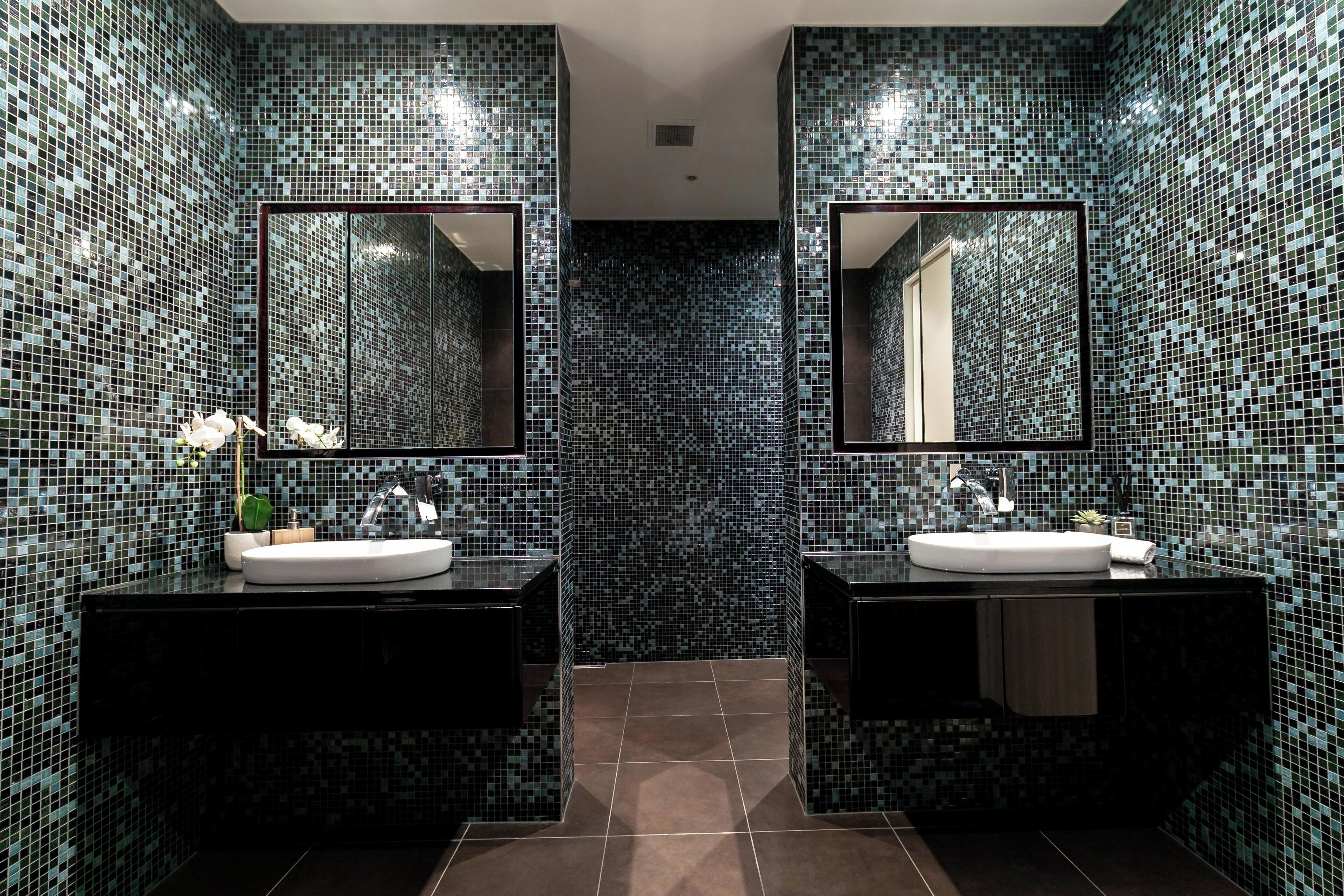A bathroom with two sinks, mirrored cabinets, and mosaic tile walls.