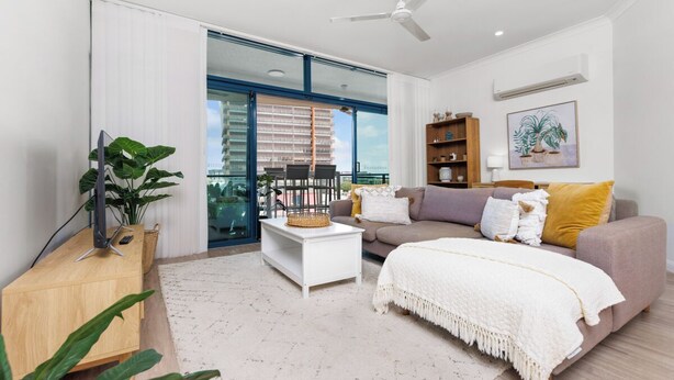 A modern living room with a sofa, coffee table, and a large window with a view of a building. - Scenic CBD Getaway, Harbour Views, Pool/Gym, Cafes (Darwin)