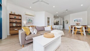 A modern living room with a sofa, coffee table, and a dining area with a table and chairs. - Scenic CBD Getaway, Harbour Views, Pool/Gym, Cafes (Darwin)