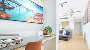 Ett modernt hotellrum med ett stort fönster, ett skrivbord med en stol, en soffa och en liten köksdel i bakgrunden.
