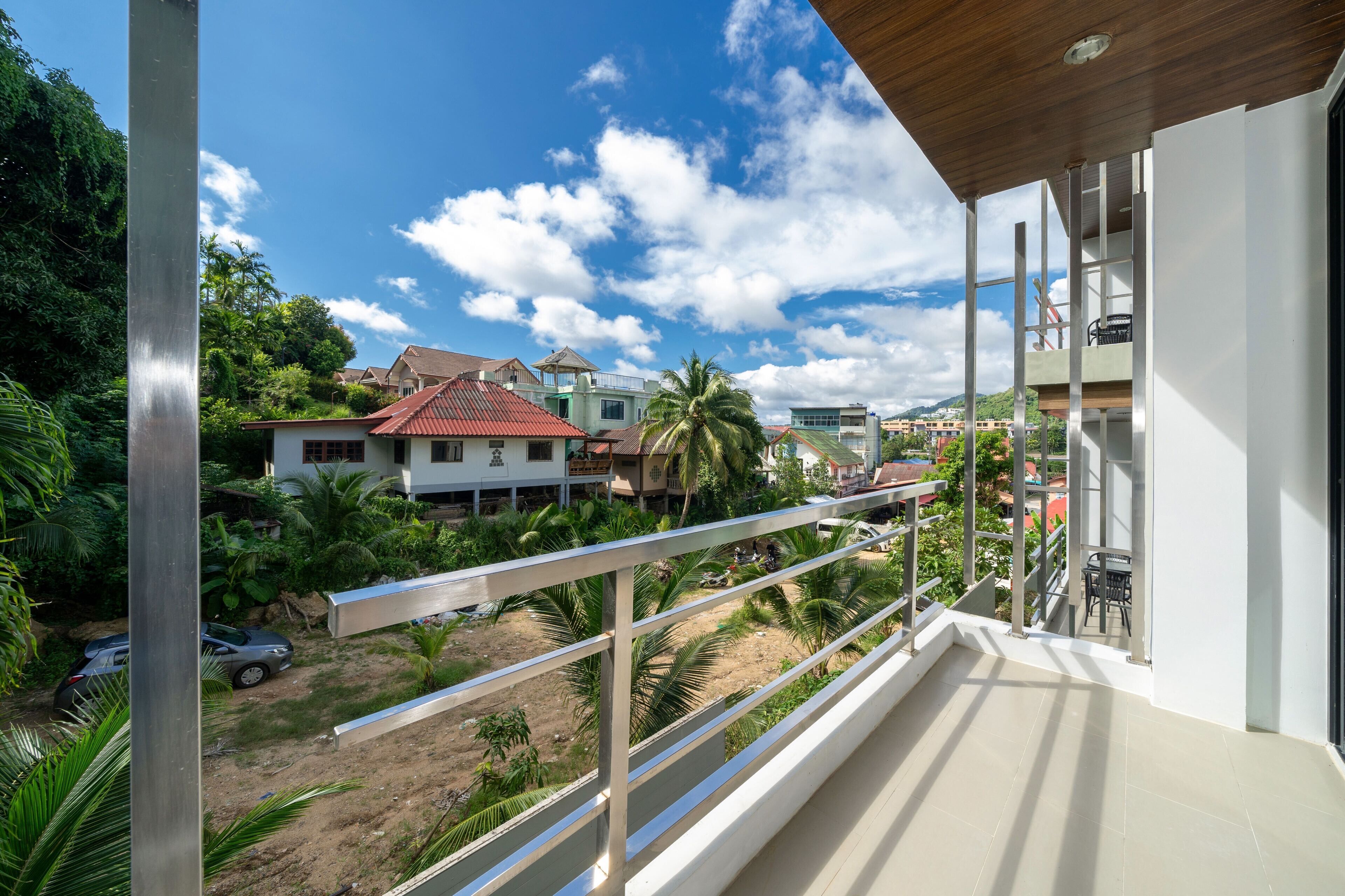 Un balcon offrant une vue sur des maisons, des palmiers et un ciel dégagé.