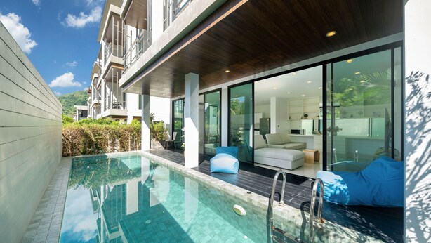 A modern pool area with a clear pool, wooden deck, and a seating area with a sofa and cushions.