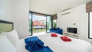 A modern hotel room with a large bed, a TV, and a balcony with a view of buildings.