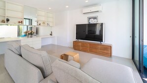 A modern living room with a grey sofa, a wooden coffee table, a flat-screen TV on a wooden stand, and a large window with a view of greenery.