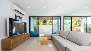 A modern living room with a flat-screen TV, a wooden cabinet, a grey sofa, and a wooden ottoman.