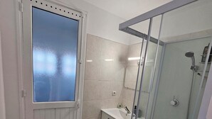 Un baño con cabina de ducha de vidrio, un lavabo blanco y una toalla verde en el suelo.