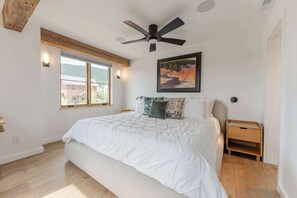 Una camera da letto con un letto, una ventola a soffitto, una finestra, un quadro e un comodino.