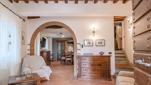A cozy living room with a brick archway, wooden furniture, and a staircase leading to another level.