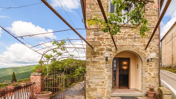 A stone building with a wrought iron gate, a stone pathway, and a view of the countryside.