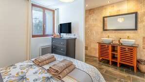 Een hotelkamer met een bed, een televisie, een badkamer met twee wastafels en een grote spiegel.