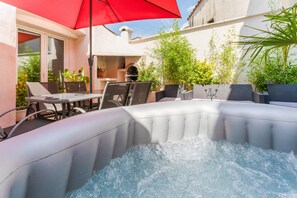 Ein Whirlpool mit rotem Sonnenschirm, Gartenmöbel und Kübelpflanzen auf einer Terrasse.