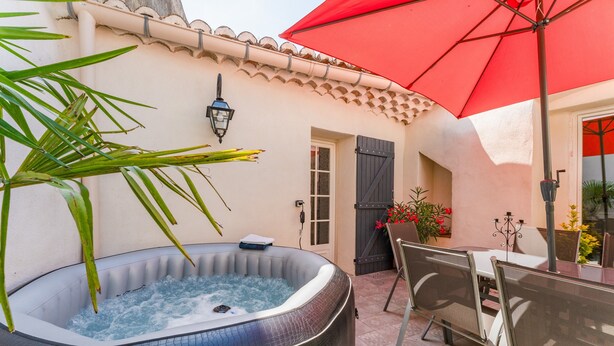 Een jacuzzi, terrasmeubilair buiten, een rode parasol en een betegeld terras.