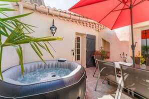 A hot tub, outdoor seating, a red umbrella, and a tiled patio. - Holiday Home ‘La Bonbonnière’ – Charm and Comfort at the Foot of Mont Ventoux (Malaucène)