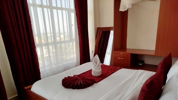 Ein Hotelzimmer mit Bett, Holz-Kopfteil, Spiegel und einem Fenster mit Vorhängen.
