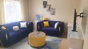 Ein Wohnzimmer mit zwei blauen Sofas, einem gelben Pouf und einem weißen Schrank.
