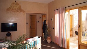 A living room with a television, a woven light fixture, a potted plant, and a sliding glass door leading to an outdoor area. - Labri de la Plage (Sidi Kaouki)