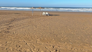 A beach with footprints, two white lounge chairs, and a blue umbrella. - Labri de la Plage (Sidi Kaouki)