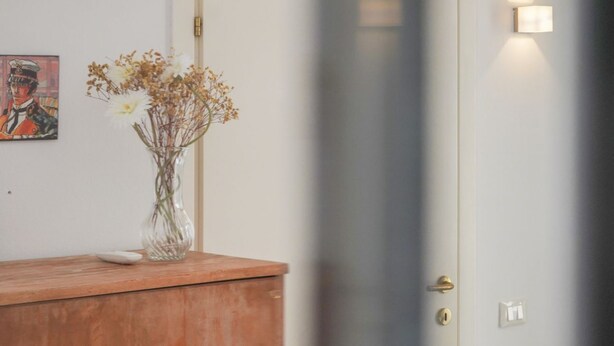 A reception area with a wooden counter, a vase with dried flowers, and a wall-mounted light fixture. - Small-scale apartment with garden (Venezia)