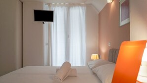 A hotel room with a bed, a television mounted on the wall, a window with curtains, and a nightstand with a lamp. - Small-scale apartment with garden (Venezia)