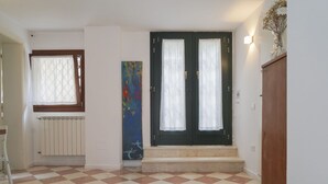 A hallway with a checkered floor, a radiator, a door with two glass panels, and a painting on the wall. - Small-scale apartment with garden (Venezia)