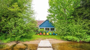Eine Holzstele führt zu einem blauen Haus, das von Grünpflanzen umgeben ist.