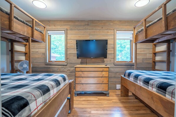 A bedroom with bunk beds, a TV mounted on the wall, and a dresser.