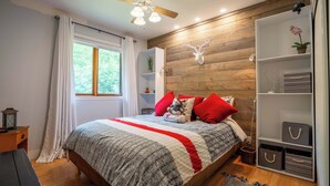 Ein Schlafzimmer mit einem Bett, einem Deckenventilator, einem Fenster mit Vorhängen, einer Holzwand und einem Bücherregal.