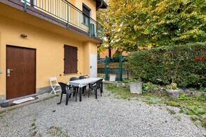 A building with a balcony, a door, and a table with chairs in the courtyard.