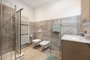 Un bagno moderno con cabina doccia in vetro, bidet, water e lavabo con portasciugamani.