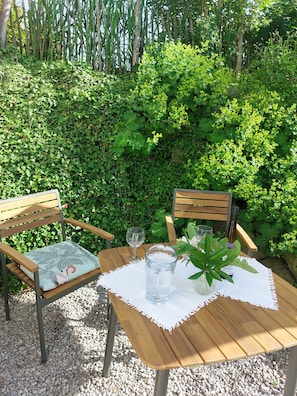 A wooden table with a white tablecloth, two chairs, a glass pitcher, two wine glasses, and a potted plant. - Apartment 'Krottenhill 2 ¼' with Sauna, Garden, and Wi-Fi (Ingenried)