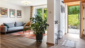 Un salon moderne avec un canapé, une plante en pot, un coin repas et une vue à travers une porte vitrée.