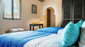 Quarto com duas camas, uma mesinha de cabeceira com abajur, um quadro na parede e uma porta com janela.