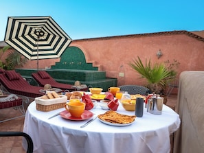 Una mesa con cosas para el desayuno, un paraguas a rayas y una piscina con sillones de descanso.