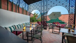 An outdoor seating area with tables and chairs, a patterned wall, and a view of a building in the background. - RIAD KSAR AGDID (Marrakech)