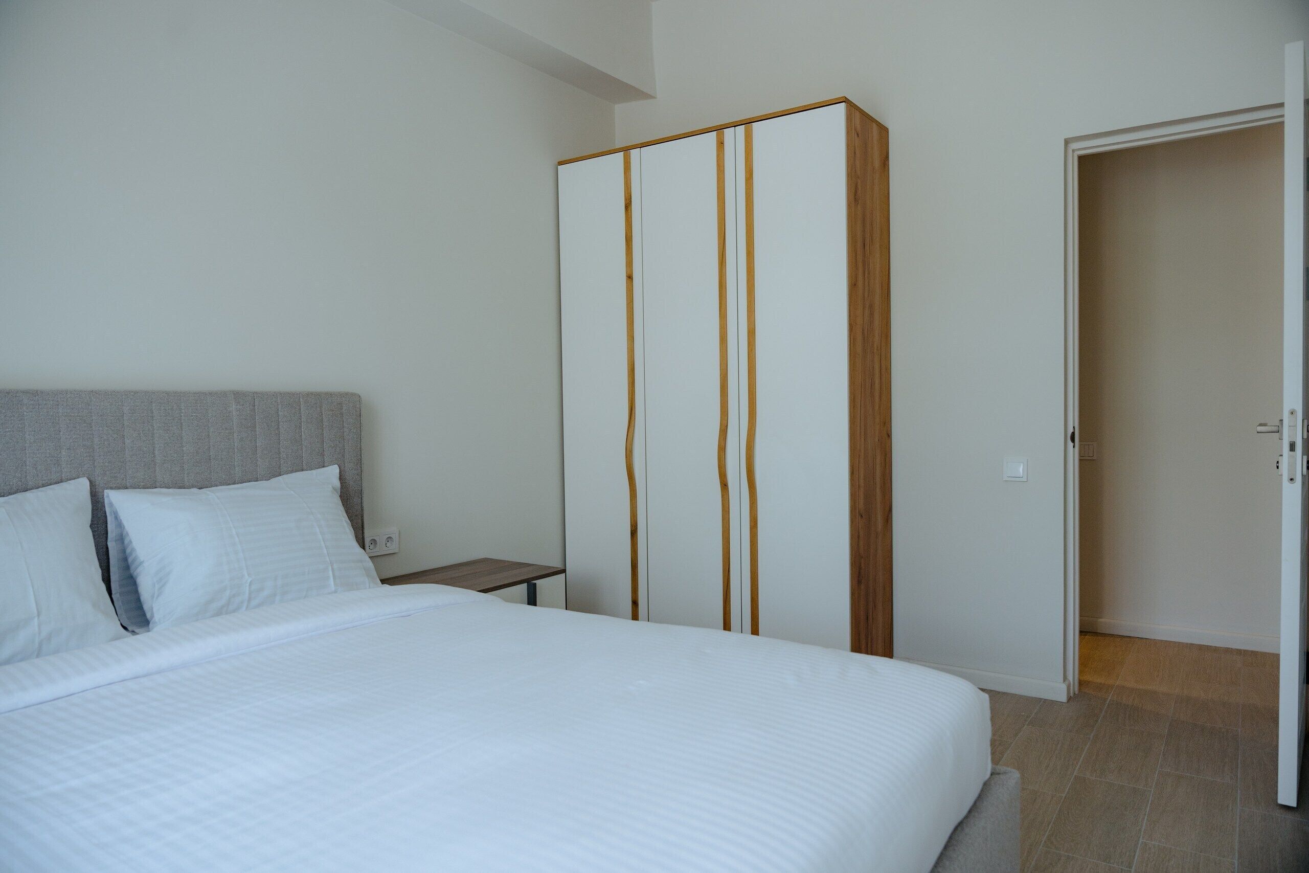 A bedroom with a bed, a wardrobe, a nightstand, and a door.